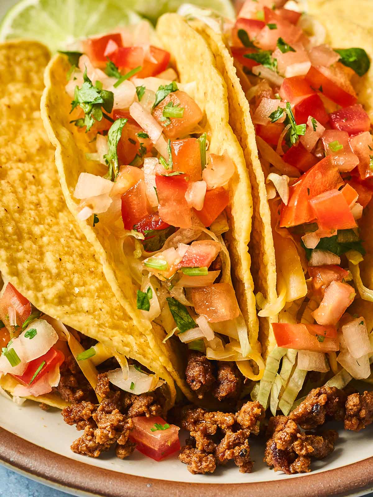 Close up photo of ground beef tacos topped with lettuce and salsa fresca.