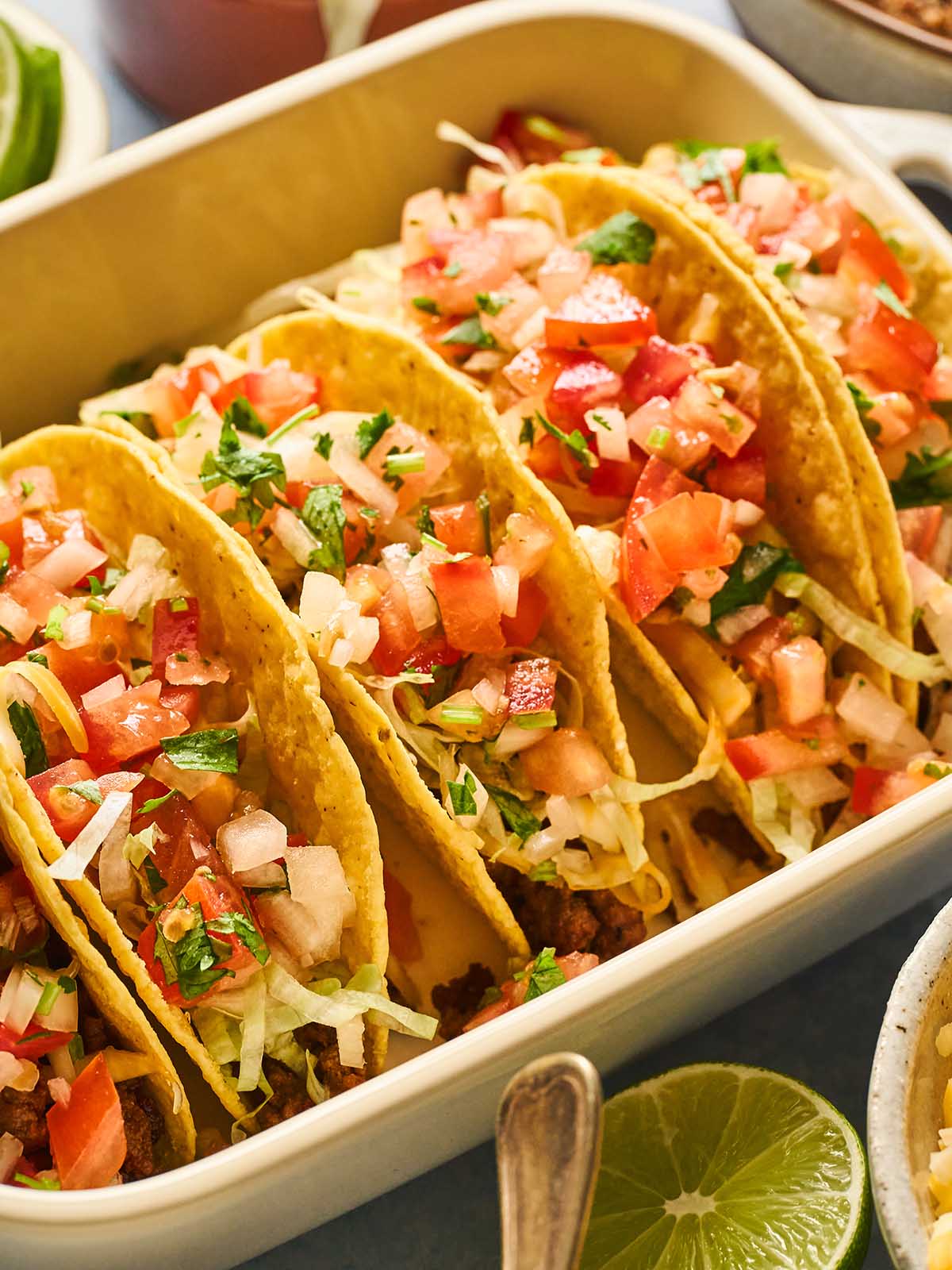 A baking dish filled with ground beef tacos topped with lettuce and salsa fresca.