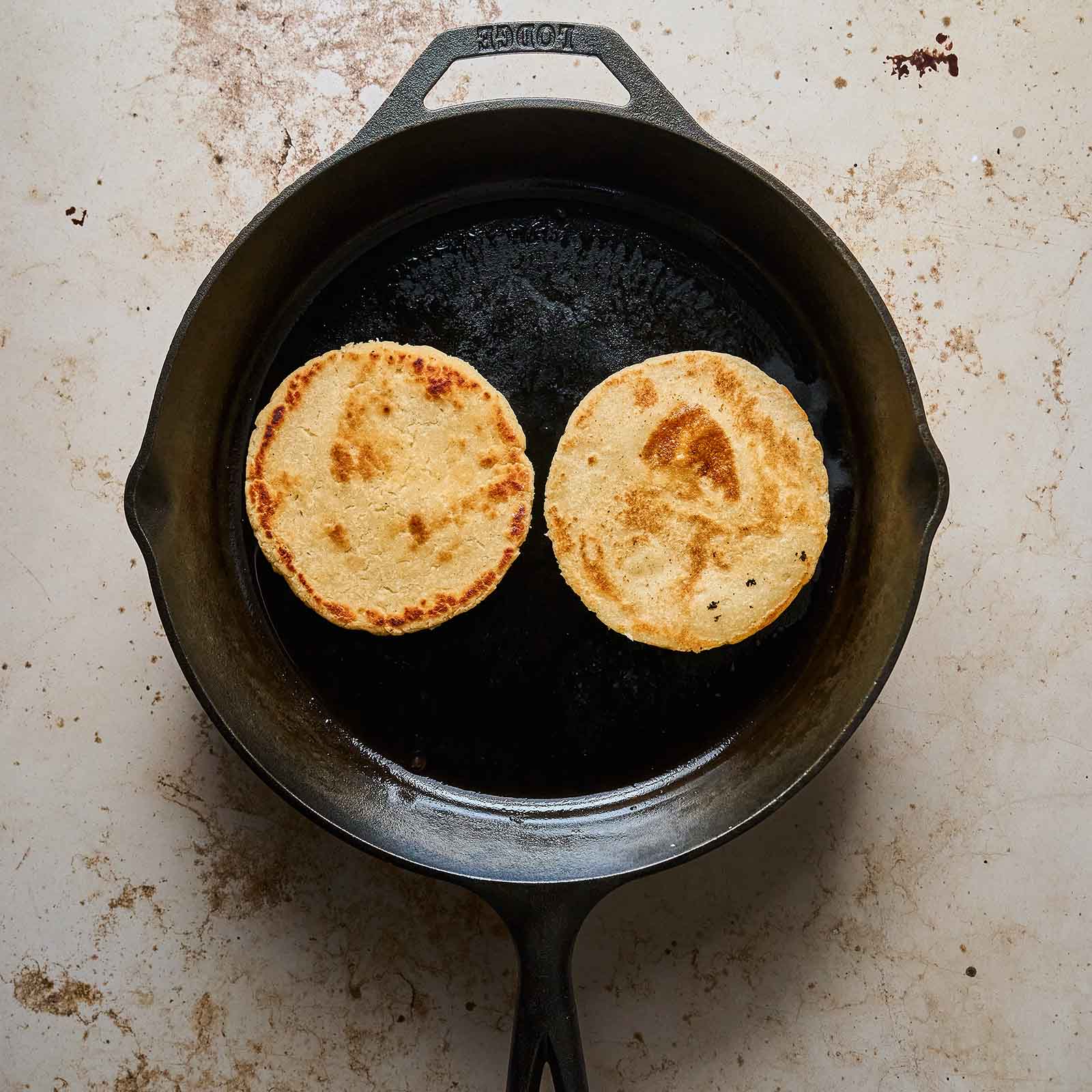 Cooking two gorditas in an iron skillet.