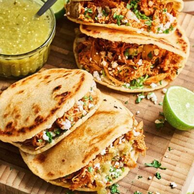Shredded meat inside gorditas topped with fresh cilantro and onions, served with lime and sides for an authentic Mexican flavor.