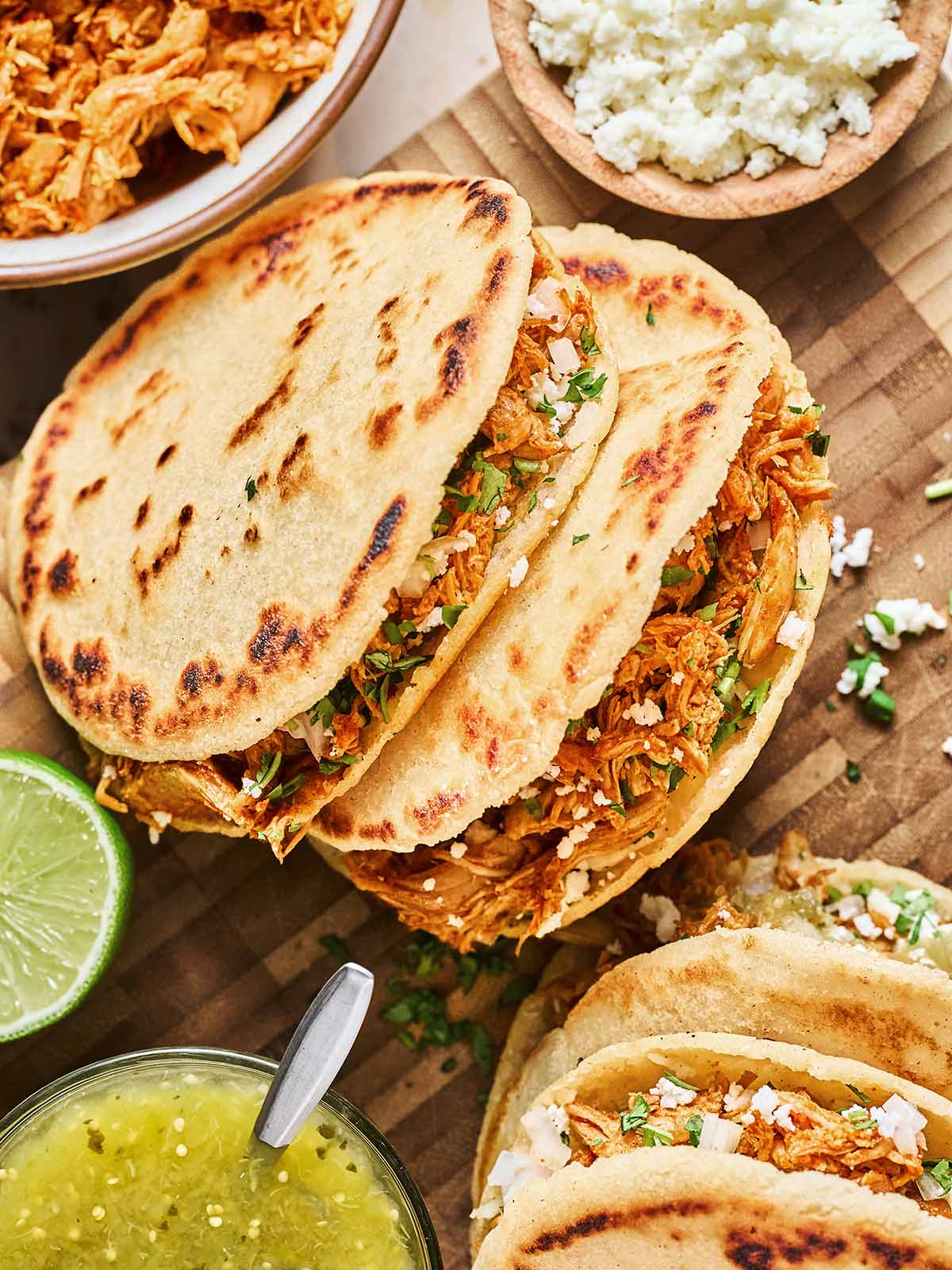 Shredded meat inside gorditas topped with fresh cilantro and onions, served with lime and sides for an authentic Mexican flavor.