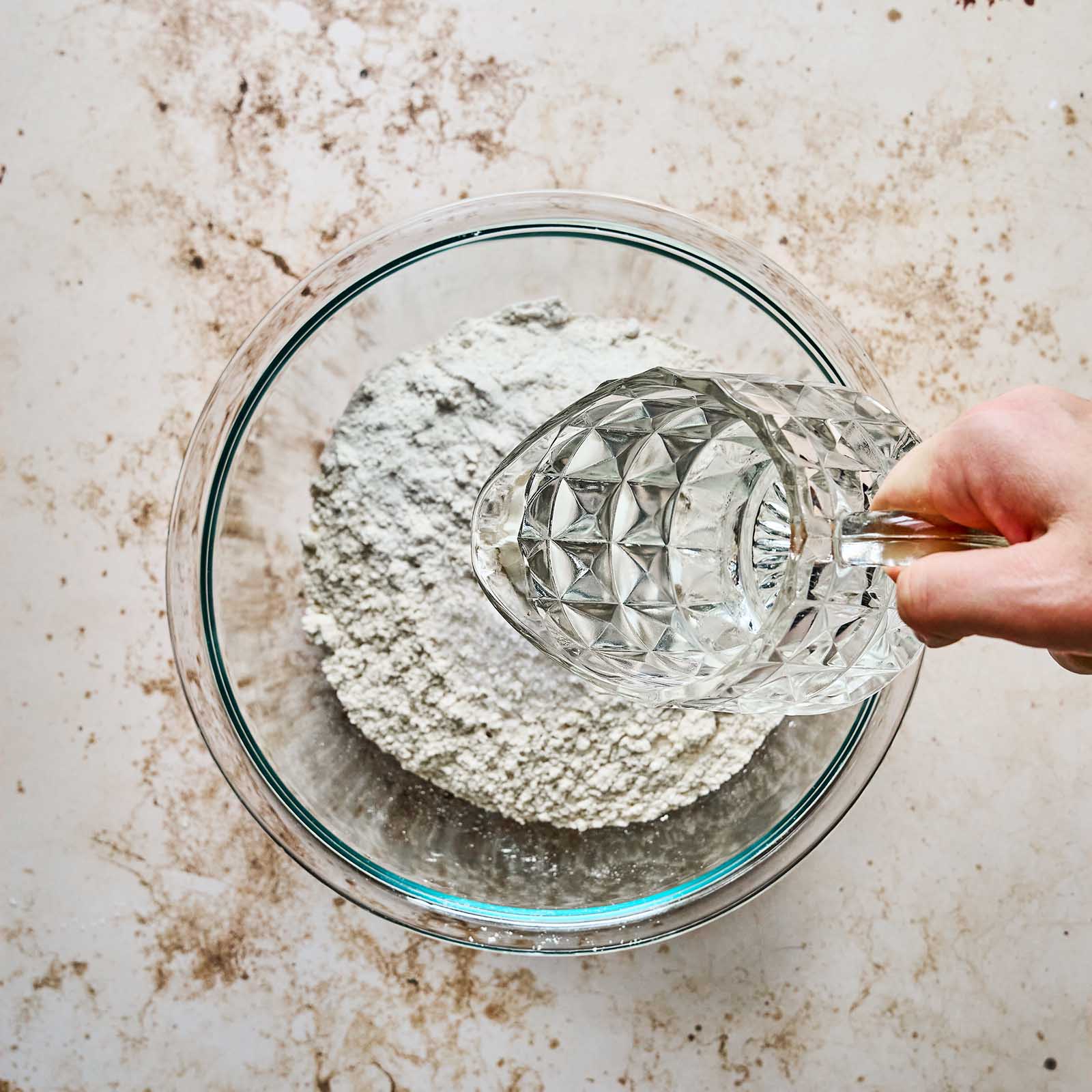Adding water with a measuring cup to a bowl with masa harina.