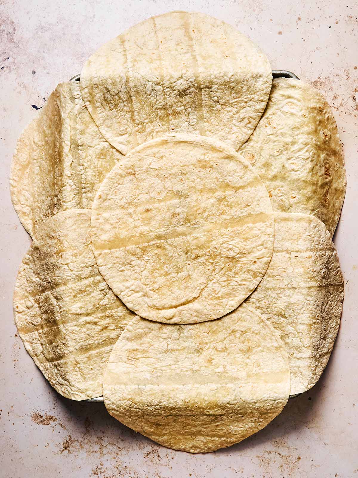 A round baking dish is lined with overlapping corn tortillas, covering the bottom and sides, on a light-colored surface.