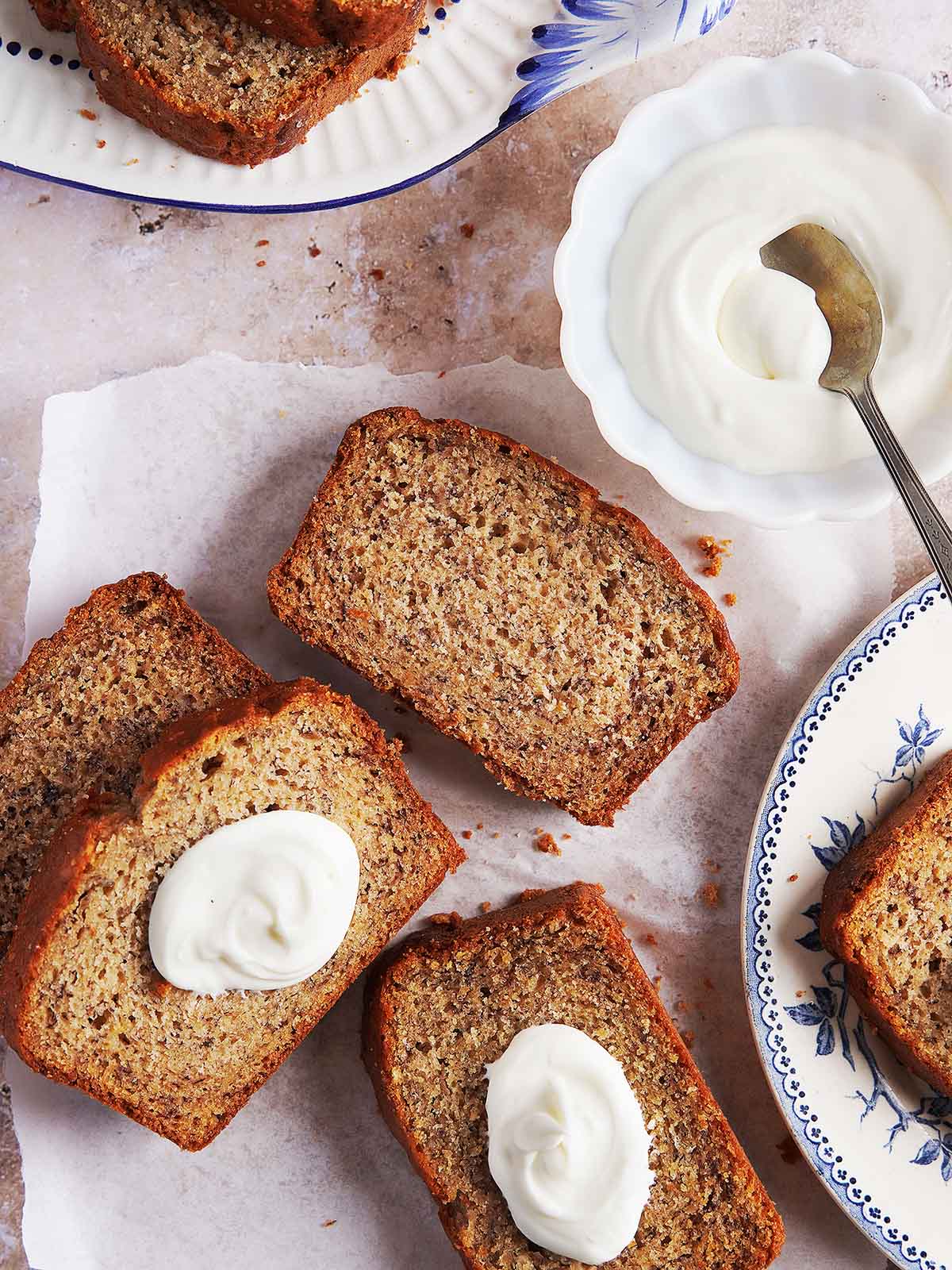 Slices of Panqué de Plátano, some topped with a dollop of cream, served alongside a small bowl of cream.