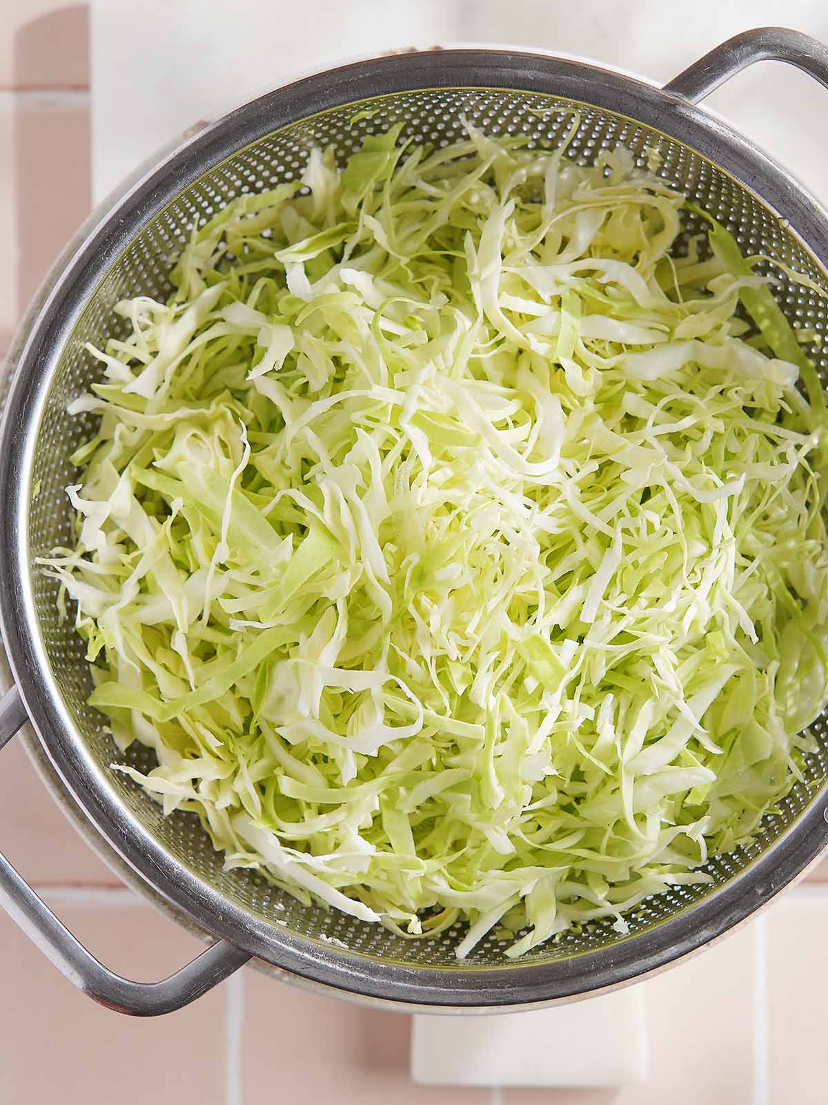 Thinly shredded cabbage in a metal colander.