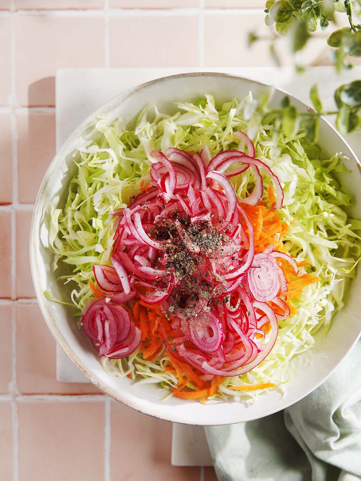 A bowl of shredded cabbage and carrots topped with thinly sliced red onions and black pepper.