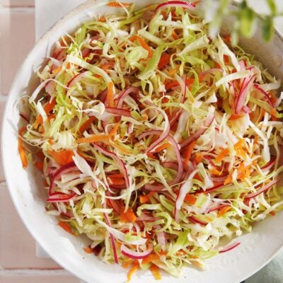 A bowl of curtido featuring shredded cabbage, julienned carrots, and sliced red onions.