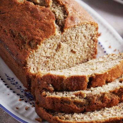 A loaf of banana bread on a patterned platter, with three slices cut and resting in front.
