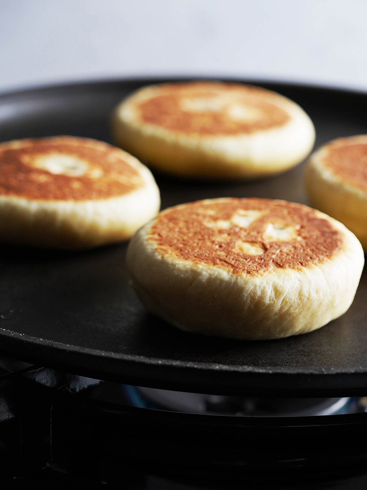 Four golden-brown gorditas cooking in a black skillet over a gas flame.