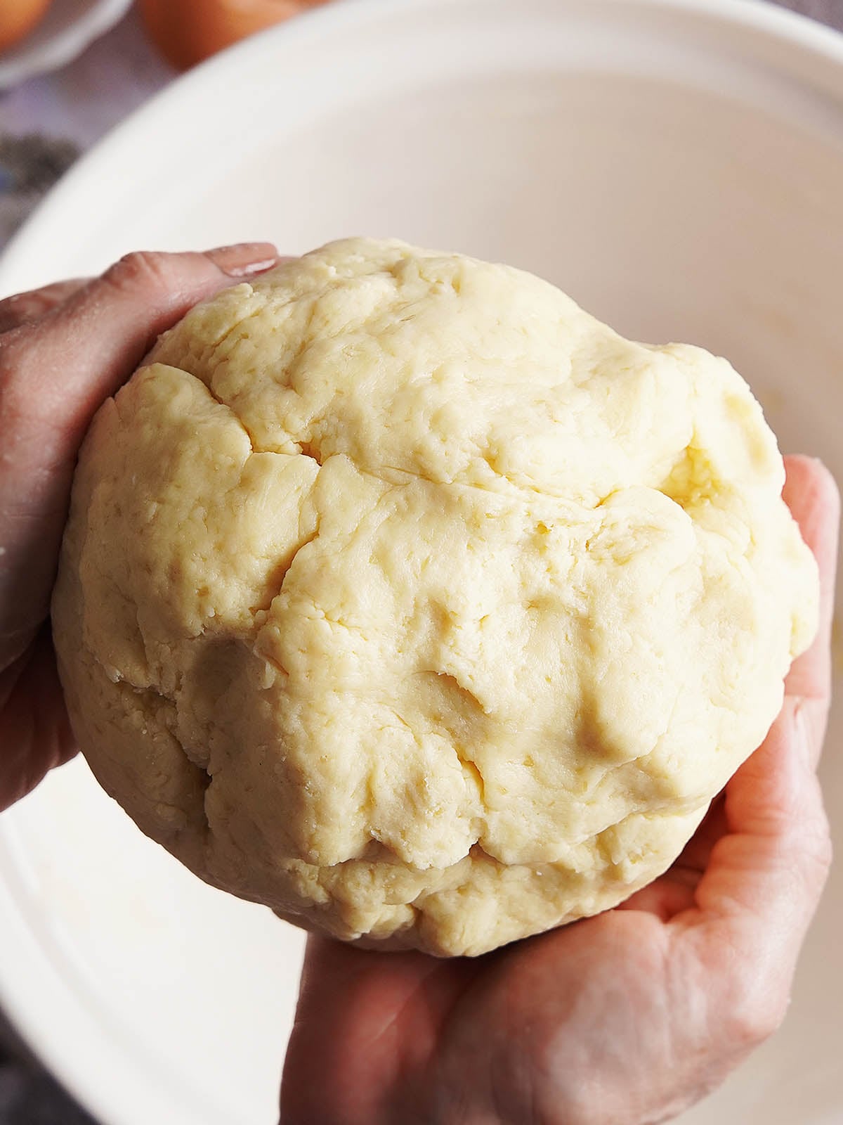 Hands holding a ball of raw pastry dough over a mixing bowl.