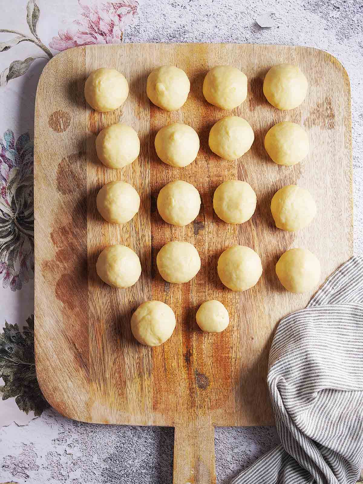 Seventeen balls of dough arranged in rows on a wooden cutting board.