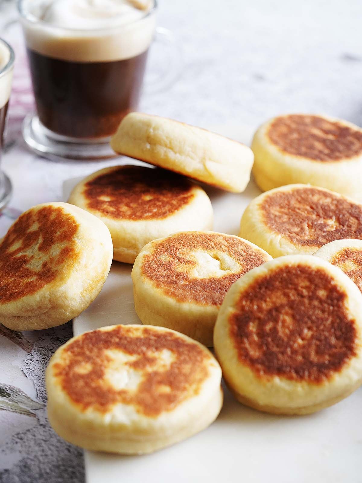 A pile of golden-brown griddle cakes next to a glass of coffee.