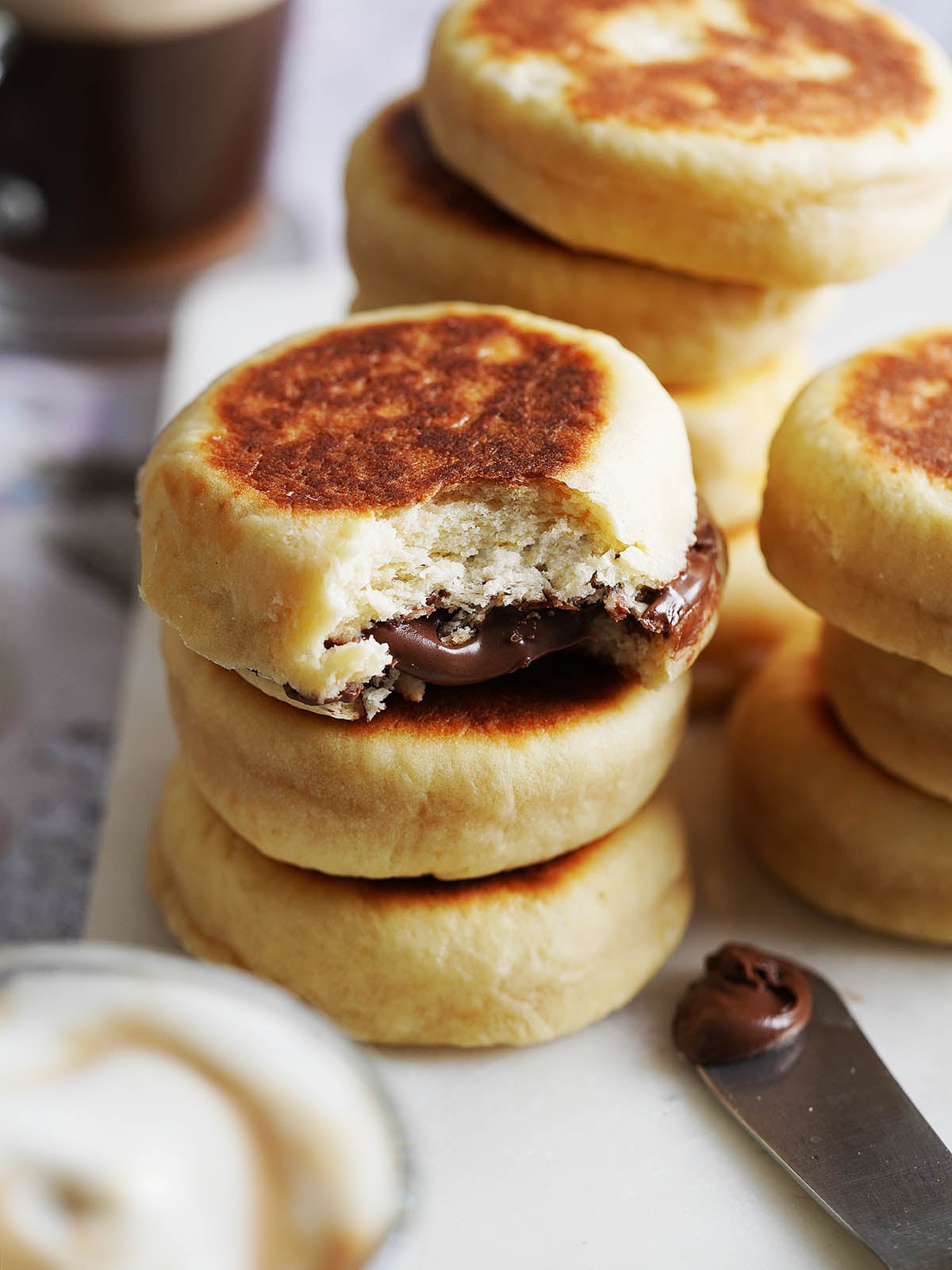 A stack of round, gorditas de nata, one with a bite taken out to reveal a chocolate spread filling, next to a knife with a smear of the spread.