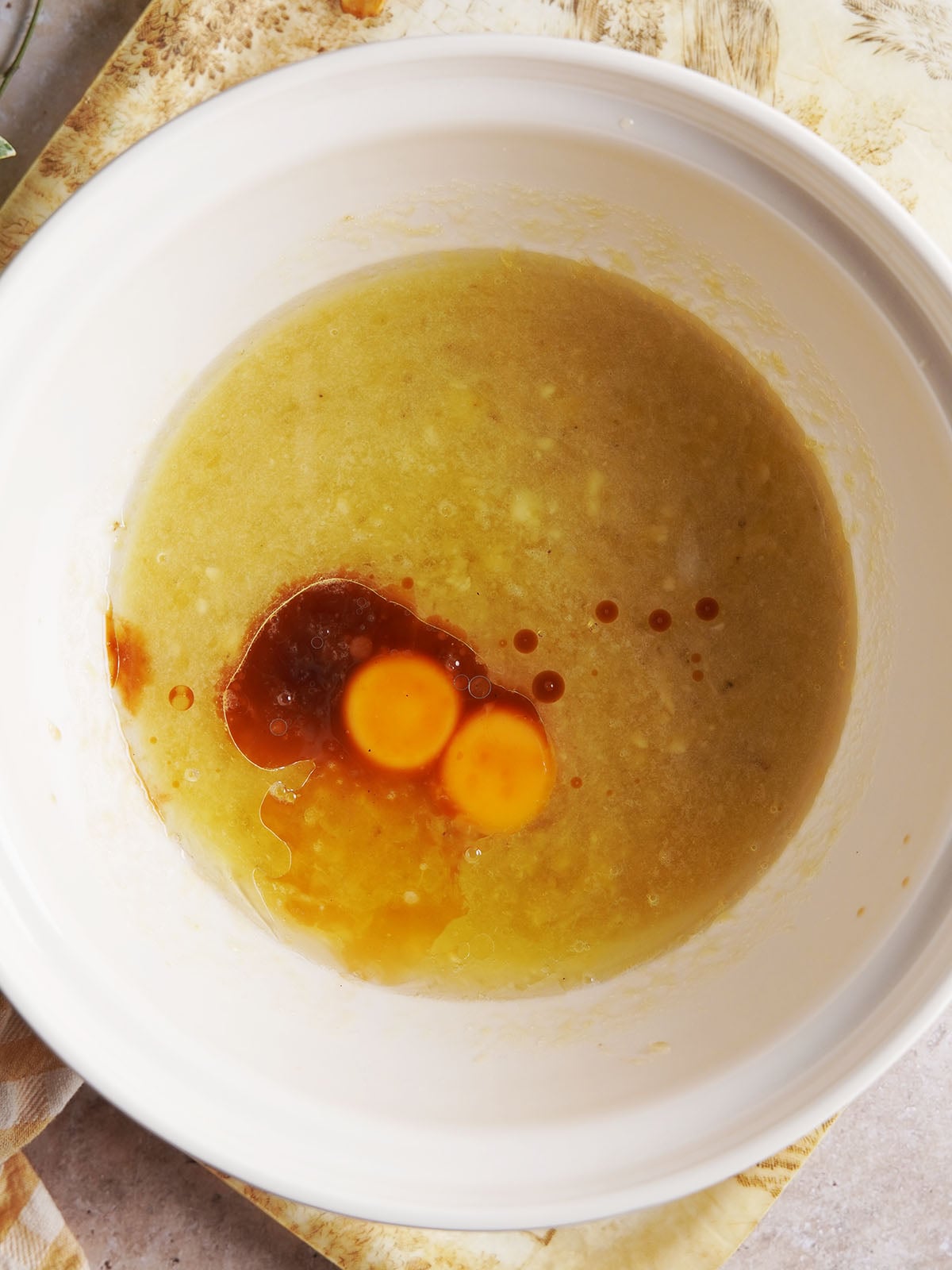 Two raw egg yolks and a splash of vanilla extract sitting in a bowl of pale yellow batter.
