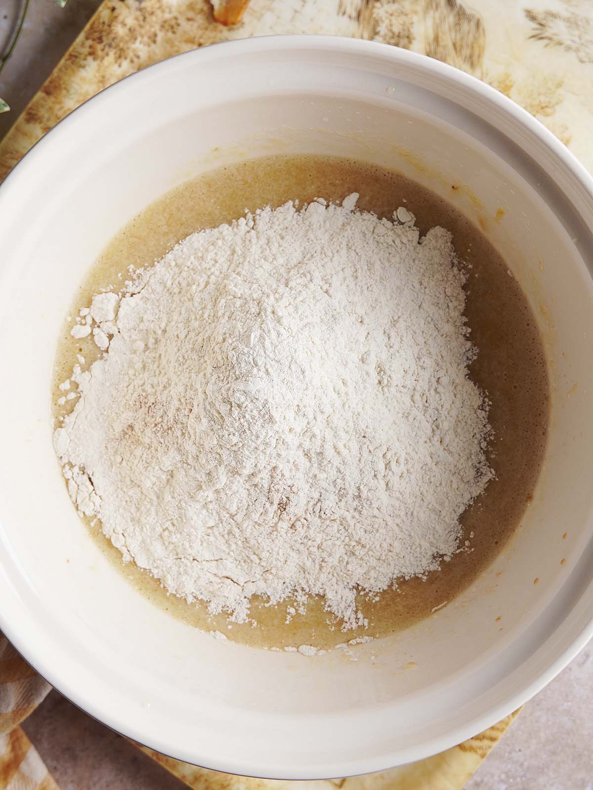 A pile of white flour sitting on top of a brown liquid batter inside a white mixing bowl.