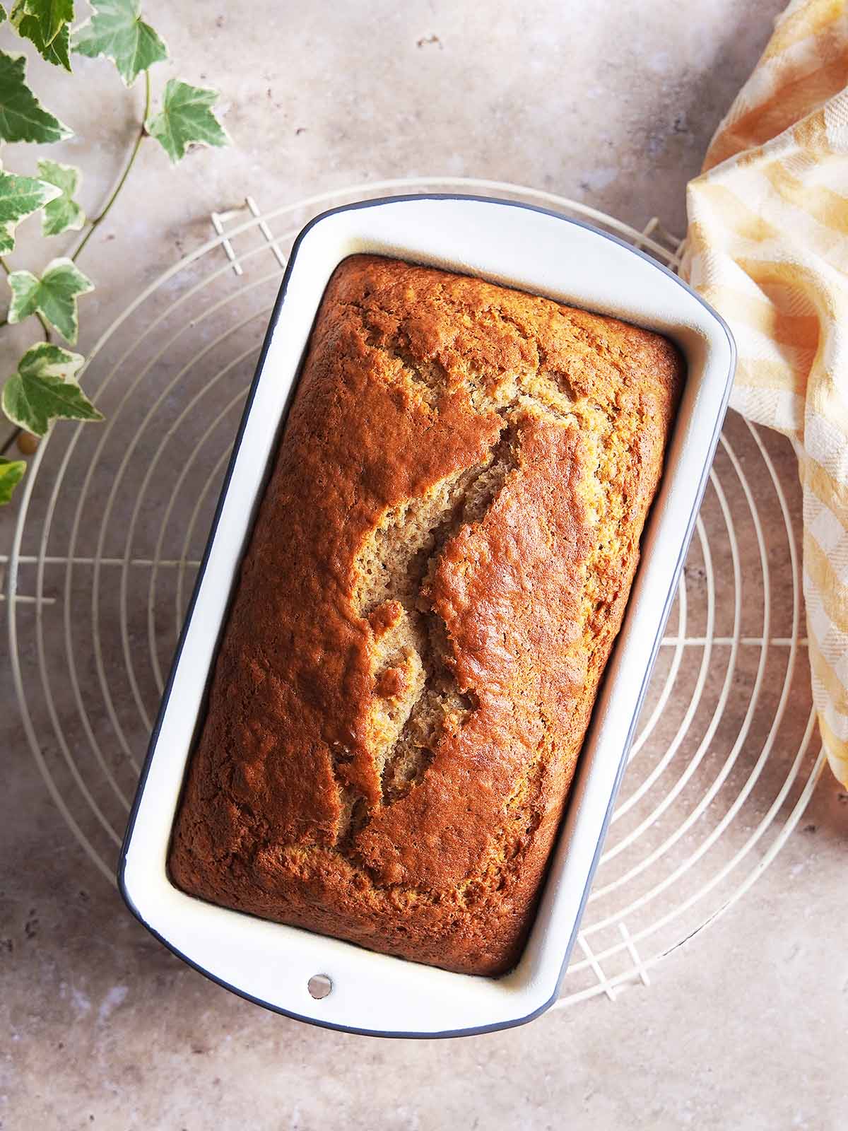 A loaf of golden-brown banana bread in a rectangular baking pan resting on a wire cooling rack.