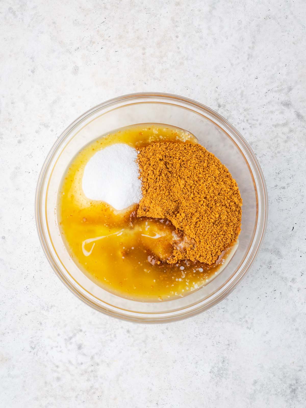 A glass bowl containing a liquid base topped with a pile of white granules and a larger pile of orange crumbs.