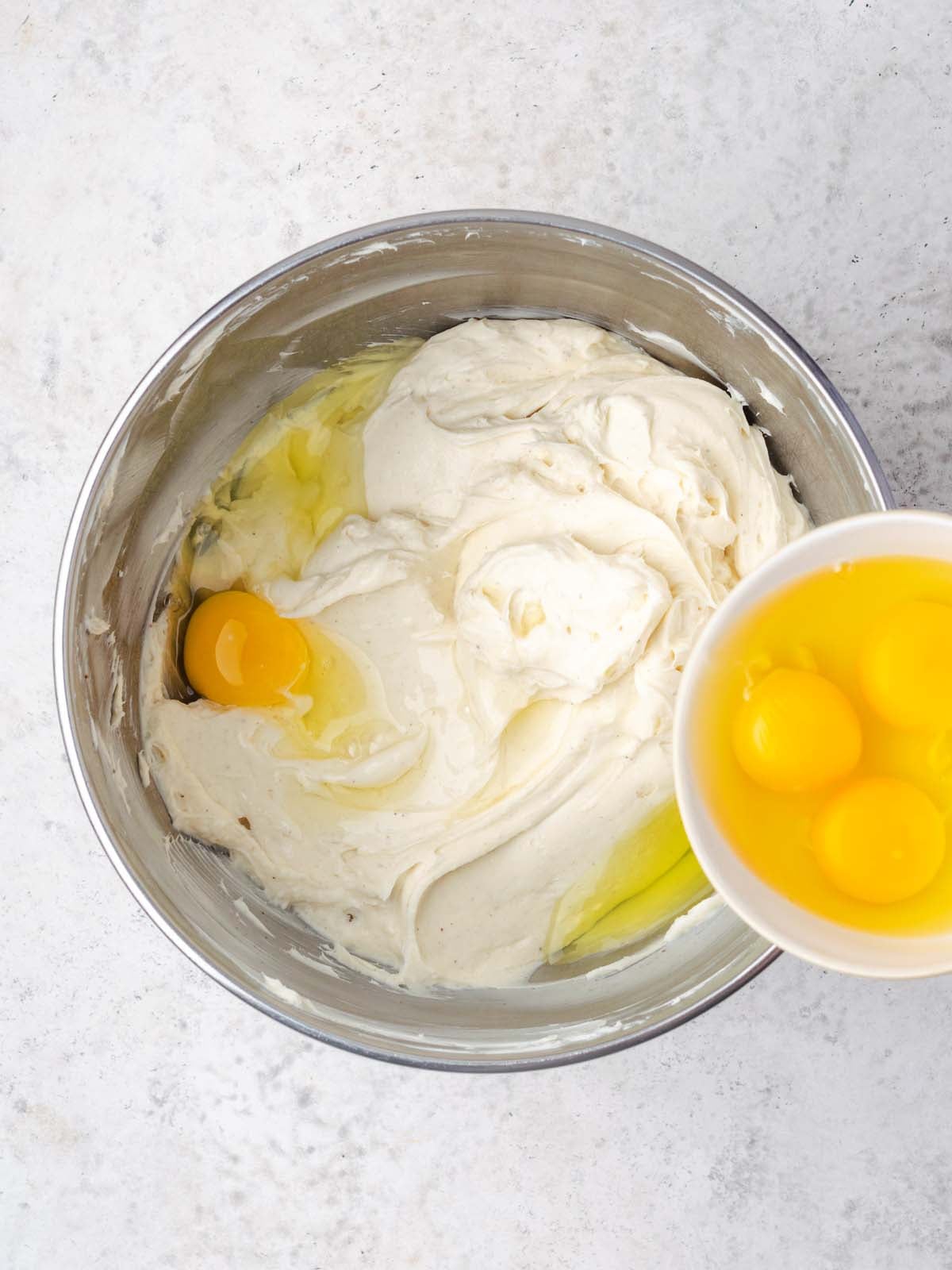 A mixing bowl containing batter with a cracked egg, next to a small bowl holding three more raw eggs.