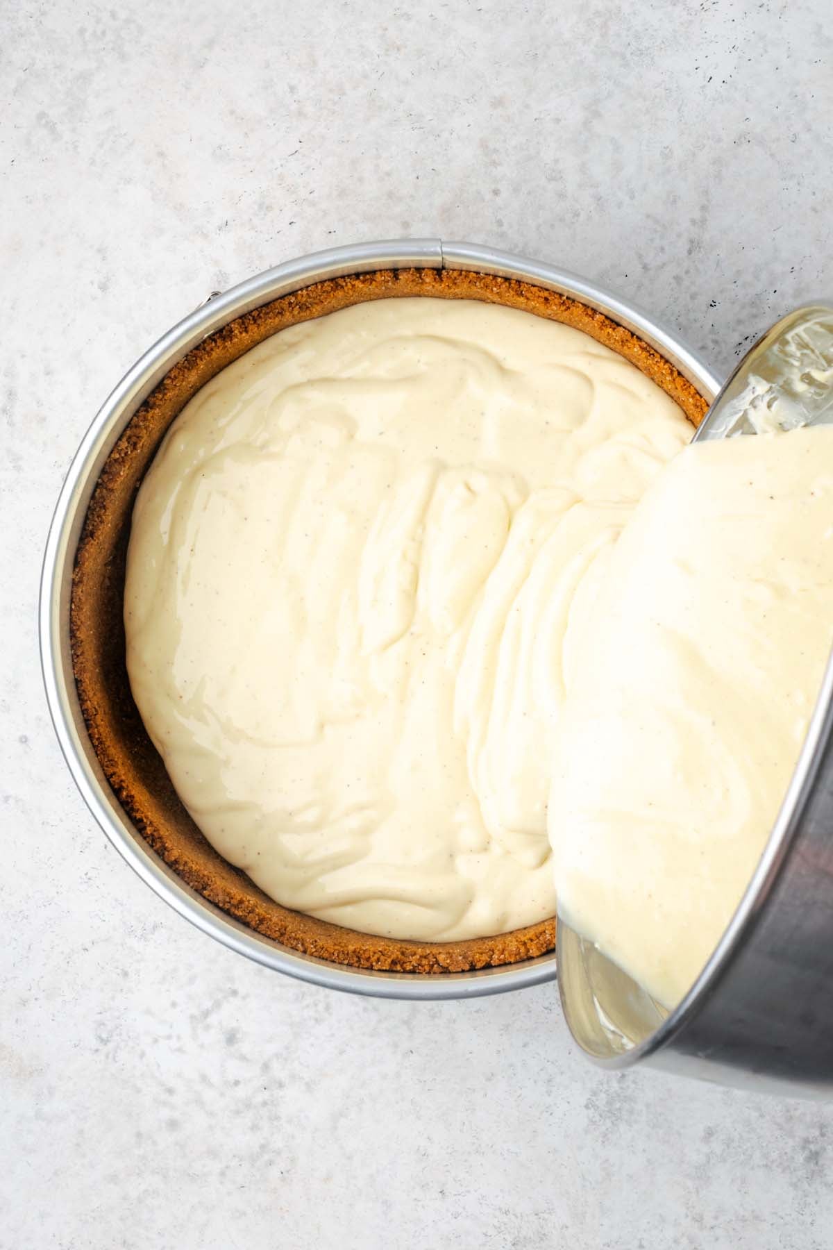 Creamy cheesecake batter being poured into a springform pan lined with a graham cracker crust.