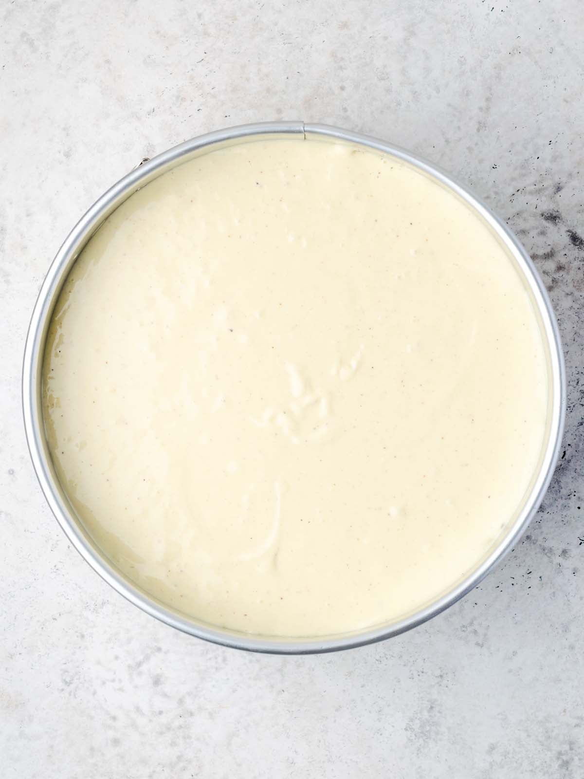 Cake batter in a round metal baking pan, viewed from directly above.